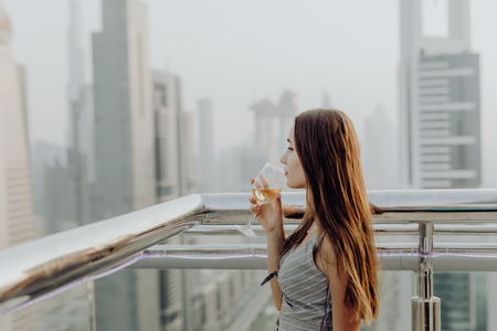 Young pretty woman drink white wine and enjoy the amazing view of Dubai downtown.の写真素材