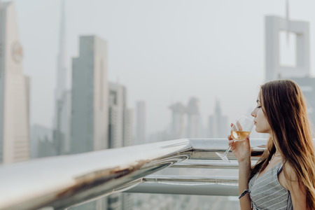 Young woman drink white wine on restaurant terrace and look enjoying the panorama view on Dubai downtown architecture.の写真素材