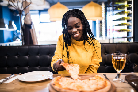 Young african american woman eating pizza in cafeの写真素材