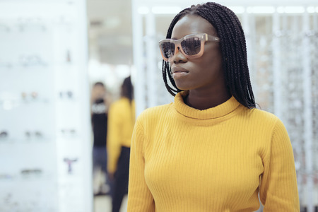 Young african woman in casual clothes try different sunglasses in optical storeの写真素材