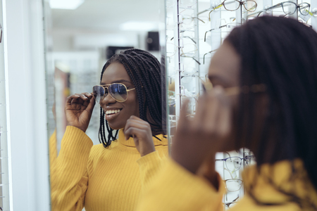 Young african woman in yellow sweater choose sunglasses in Ootician's shopの写真素材