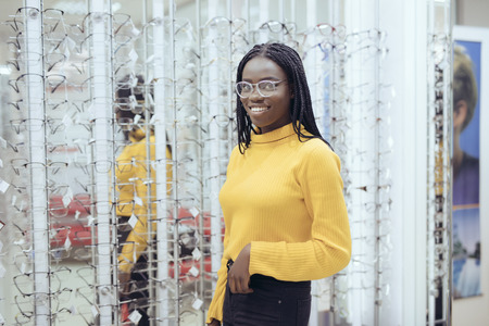 Young african woman choosing eyeglasses frames in Optician's shop.の写真素材