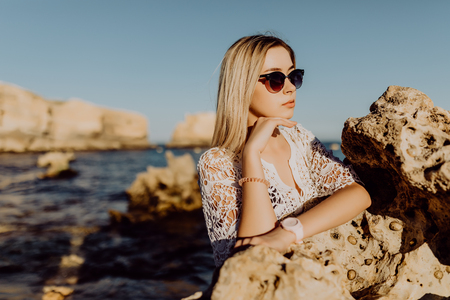 Portrait of active funny girl on the ocean with flying hair at camera and charming smile on beach with white sand and rocks backgroundの写真素材