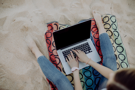 Close-up of a beautiful smiling girl on the beach working on a laptopの写真素材