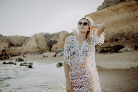 Hipster trendy woman in casual summer dress walking by the waterline and look to the waves on sea sand beach sunset or ocean sunrise.の写真素材