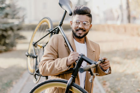 Bearded indian hipster man with a fixie bicycle. Low angle view of confident young bearded man...