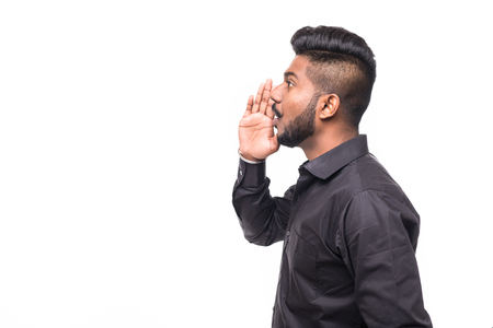 Portrait of Indian guy shouting loud, mouth open and hand cupped beside. Asian man standing on plain background with shadow and copy space. Handsome male model.の写真素材