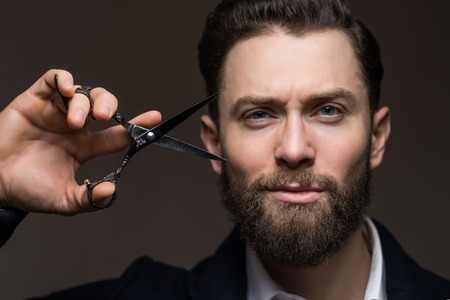 Portrait of stylish man with beard holding scissors near face. Barber scissors and straight razor, barber shop.の写真素材