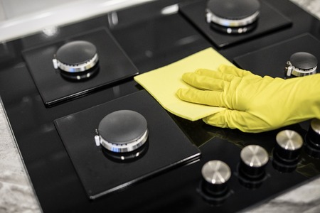 Woman hand with a yellow microfiber cloth rubs a glass ceramic stove in the kitchen.の写真素材