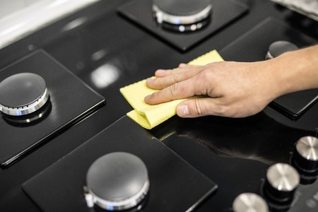 Young Men in rubber protective cleaning and polish cooker. Black shiny surface of kitchen top, hands, detergent. Set cleaning conceptの写真素材