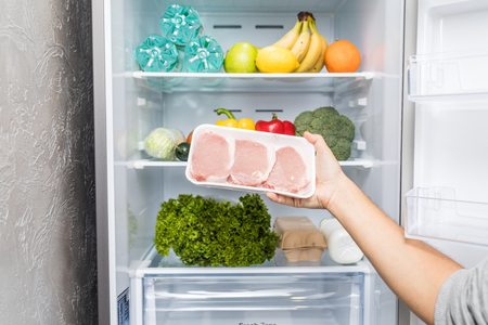 Hands take meat standing next to the open fridge.の写真素材