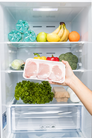 Hands take meat standing next to the open fridge.の写真素材