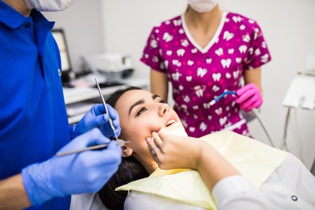 young woman patient at dentist, holding hand on cheek, showing pain, horizontal shotの写真素材