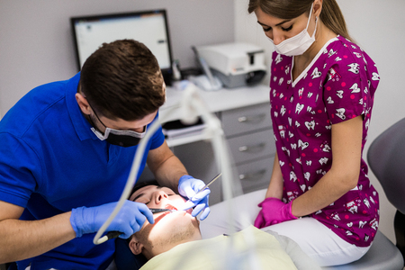 Male dentist with assistant examining girls teeth in the dentists chairの写真素材