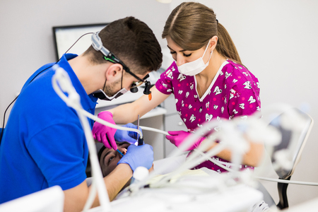 Male dentist with assistant examining girls teeth in the dentists chairの写真素材