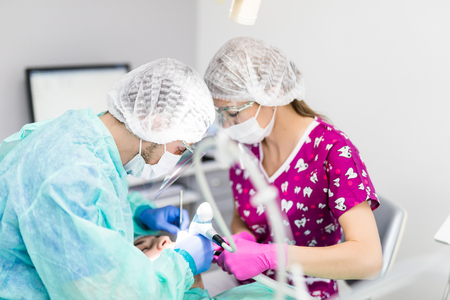 doctor operating man in cabinet with eyes closed during procedure made by dentist and assistant.の写真素材