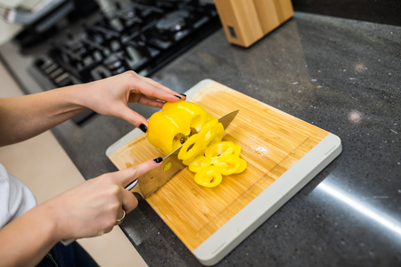 Happy young woman cutting fresh vegetables in kitchenの写真素材