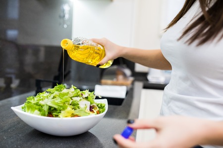 close up of young woman dressing vegetable salad with olive oil at home