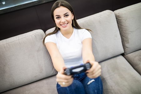 Young female playing video-games concentrating on sofa at homeの写真素材