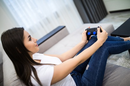Young female playing video-games concentrating on sofa at homeの写真素材