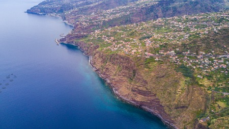 Aerial panoramic cityscape view of the cities in madeira with houses in front of tree covered mountains and white cloudsの写真素材