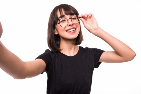 Smiling young woman casualy dressed standing isolated over white background, taking a selfie with...