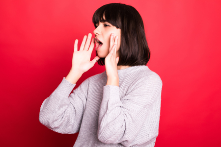 Portrait of excited screaming young woman standing isolated over red backgroundの写真素材