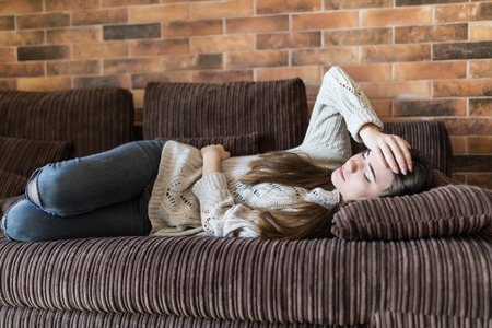 Young woman suffering from stomachache on sofa at homeの写真素材