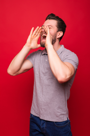 Portrait of a cheerful young man dressed in denim jacket standing isolated over red background, screamingの写真素材