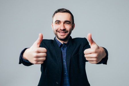 Portrait of excited man with opened mouth dressed in formal wear giving thumbs-up against gray backgroundの写真素材