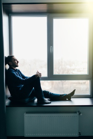 Handsome young man sitting on windowsill
