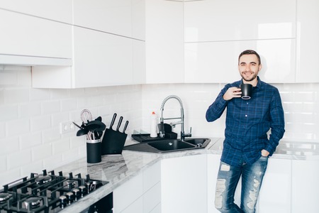 Young man smiling and holding coffee in the kitchenの写真素材