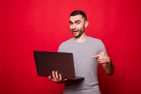 Cheerful bearded guy pointing at laptop screen over red backgroundの写真素材
