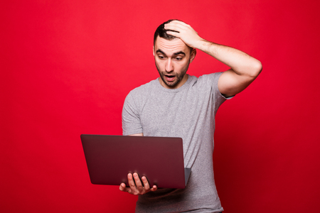Young shocked man using laptop shocked isolated on red backgroundの写真素材