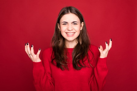 Close up isolated portrait of young annoyed angry woman holding hands in furious gesture on red...