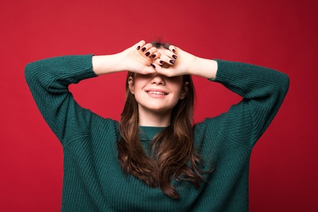 Joyful brunette woman in sweater, looking at the camera over red background