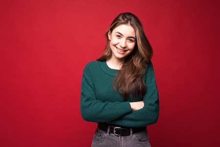 Portrait of young woman in green sweater holding hands crossed, looking aside isolated on bright red...