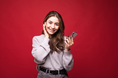 Young charming woman listening music in earphones on mobile phone, enjoy, relax, isolated on red background. People, sincere emotions, lifestyle concept.の写真素材