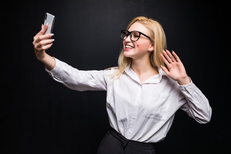 Closeup of beautiful business woman making selfie photo or have video call on isolated black background and looking at cameraの写真素材