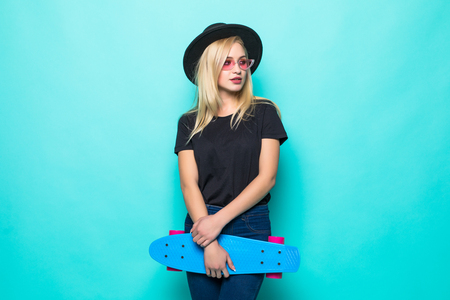 Young girl in black fluffy hat holding a skateboard and looking at the camera isolated on green backgroundの写真素材