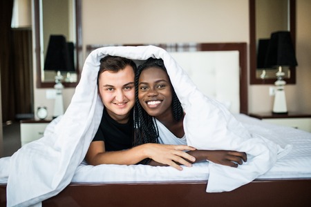Smiling young couple lying under the coverlet in bedの写真素材