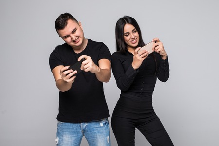 Portrait of young couple standing with mobile phone playing games standing near and looking at...
