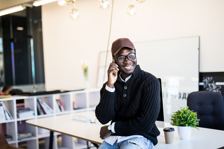 Mobile phone talk. Young black businessman has mobile phone call in modern white office interior.の写真素材