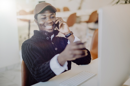 African American businessman on the phone sitting at the computer in his officeの写真素材
