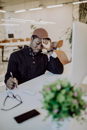 Stress, fatigue overwork. Tired African American employee in formal wear holding eyeglasses, rubbing his eyes and massaging nose bridge to release tension after long working hours in officeの写真素材