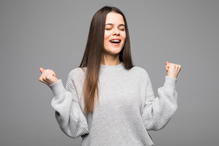 Happy girl in gray sweater with her fists up, isolated on whiteの写真素材