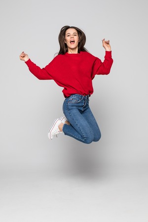 Full length portrait of a laughing woman jumping over gray background. Looking at cameraの写真素材