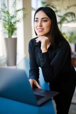 Concentrated young beautiful businesswoman working on laptop in bright modern officeの写真素材