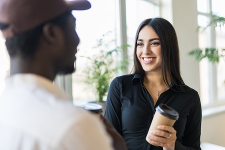 Smiling mixed race colleagues in casual clothes have informal meeting while drinking coffee in modern officeの写真素材