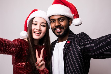 Happy asian couple with santa hat taking selfie on phone isolated on white backgroundの写真素材